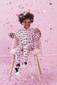 Bambina di pelle nera sorridente seduta su una sedia rosa in una stanza rosa con coriandoli rosa